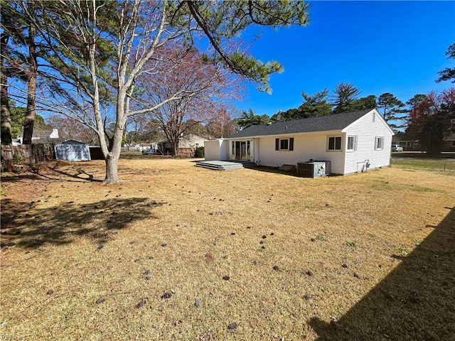 rear view of house featuring fence, central AC, a lawn, a storage shed, and an outbuilding