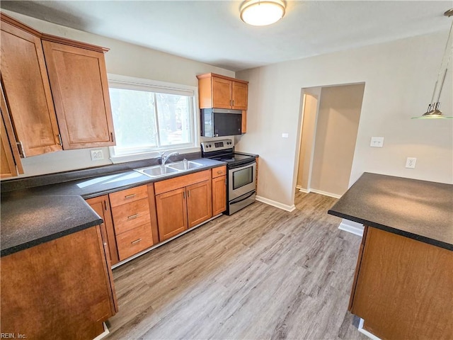 kitchen with dark countertops, stainless steel electric range oven, light wood-style floors, and a sink