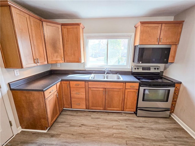 kitchen with dark countertops, light wood finished floors, appliances with stainless steel finishes, and a sink