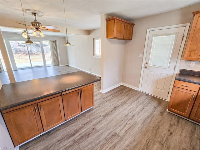 kitchen featuring brown cabinetry, baseboards, light wood-style flooring, ceiling fan, and dark countertops