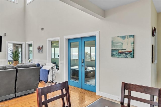 dining area featuring a towering ceiling, french doors, light wood-style flooring, and wainscoting