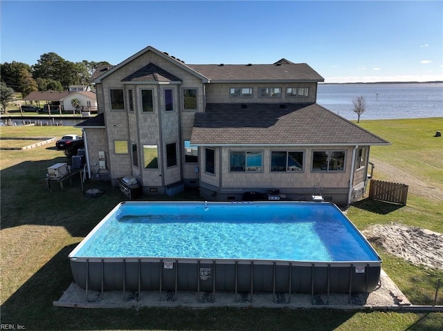 rear view of property featuring an outdoor pool, a yard, a water view, and fence