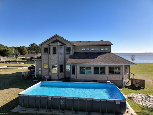 rear view of property featuring a yard, fence, an outdoor pool, and a water view