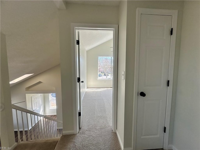 hallway featuring baseboards, carpet floors, and vaulted ceiling