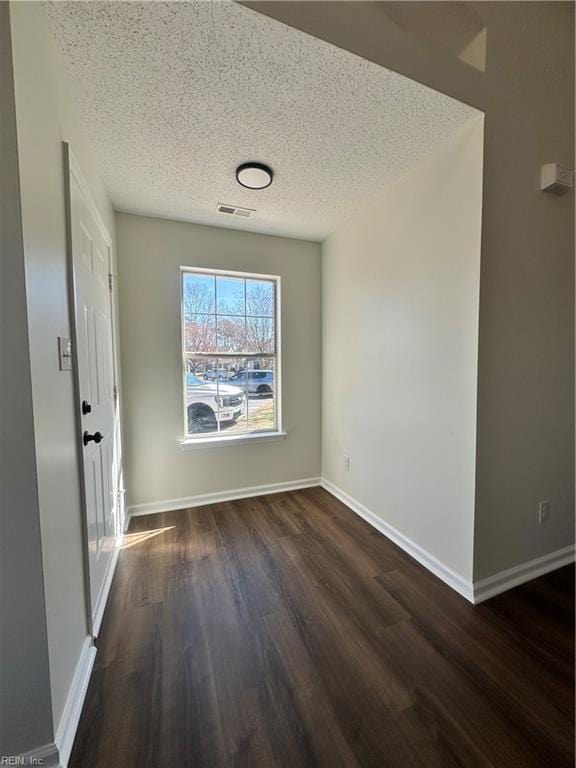 interior space featuring visible vents, a textured ceiling, baseboards, and dark wood-style flooring