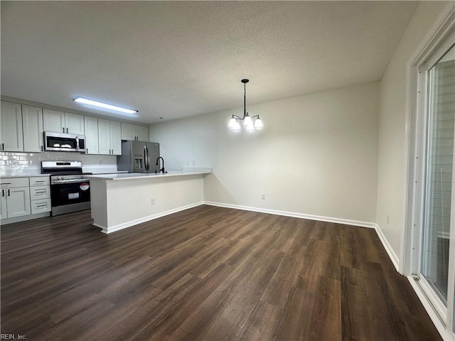 kitchen featuring a chandelier, light countertops, appliances with stainless steel finishes, a peninsula, and dark wood-style floors