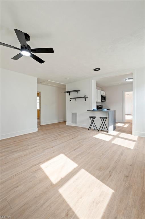 unfurnished living room with light wood finished floors, visible vents, a ceiling fan, and baseboards