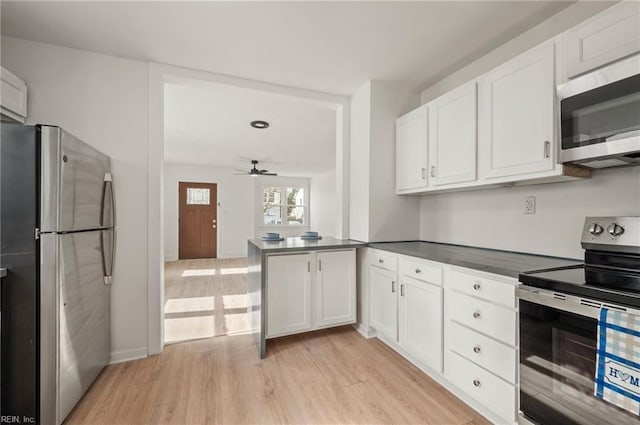 kitchen with a peninsula, light wood-style flooring, stainless steel appliances, white cabinets, and dark countertops