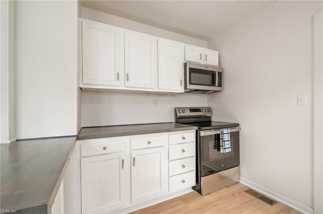 kitchen with light wood-type flooring, visible vents, stainless steel appliances, white cabinets, and baseboards