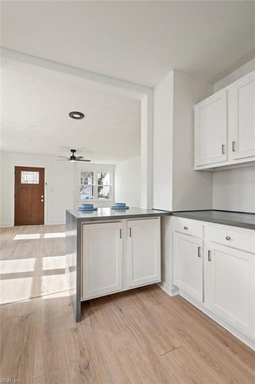 kitchen with dark countertops, a peninsula, white cabinets, light wood finished floors, and ceiling fan