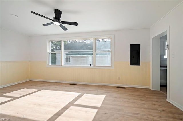 empty room featuring wood finished floors, visible vents, electric panel, ceiling fan, and wainscoting