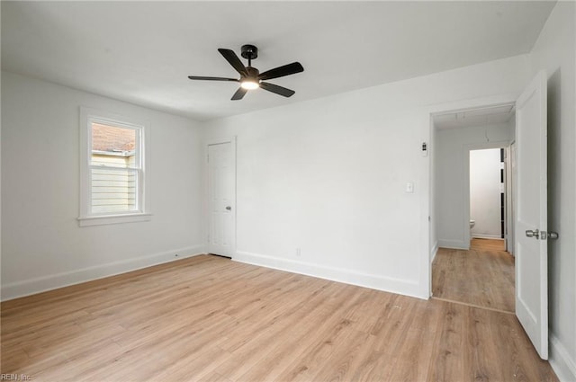 empty room featuring attic access, light wood-style flooring, a ceiling fan, and baseboards