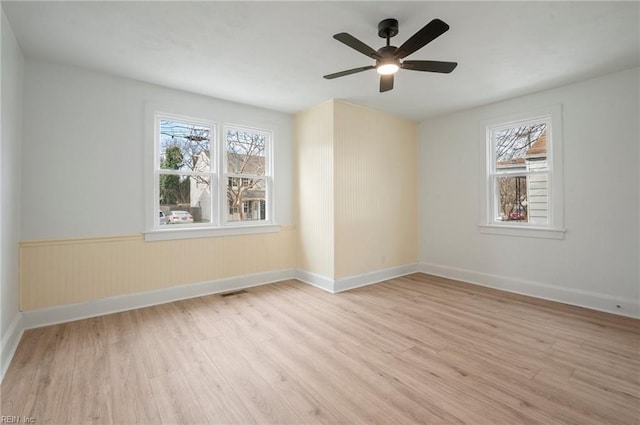 spare room with light wood finished floors, baseboards, a wealth of natural light, and wainscoting