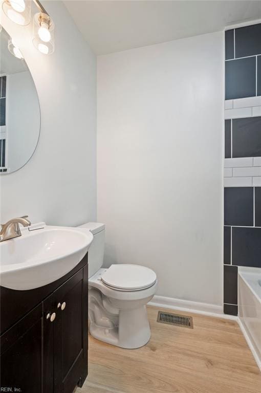 bathroom with visible vents, toilet, a washtub, wood finished floors, and vanity