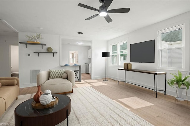 living room with a ceiling fan, light wood-style flooring, baseboards, and visible vents