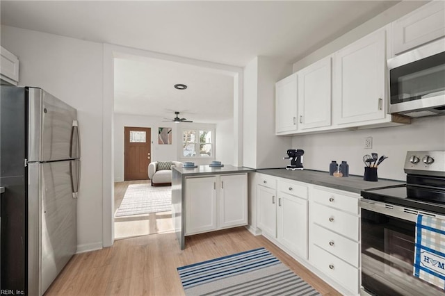 kitchen featuring dark countertops, light wood-style flooring, appliances with stainless steel finishes, a peninsula, and white cabinets