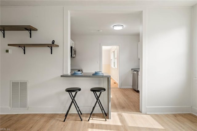 kitchen featuring visible vents, a kitchen bar, light wood-style floors, and open shelves