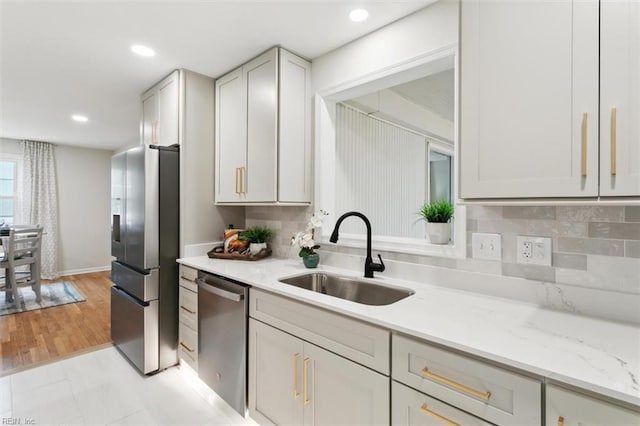 kitchen featuring light stone countertops, recessed lighting, a sink, appliances with stainless steel finishes, and backsplash