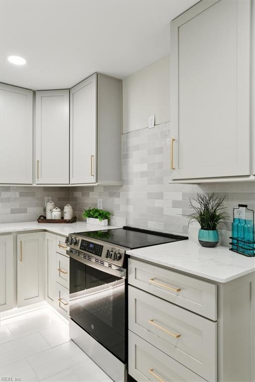 kitchen with backsplash, light stone countertops, stainless steel electric stove, and white cabinetry