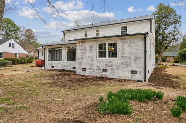 back of house with brick siding, crawl space, a chimney, and heating fuel