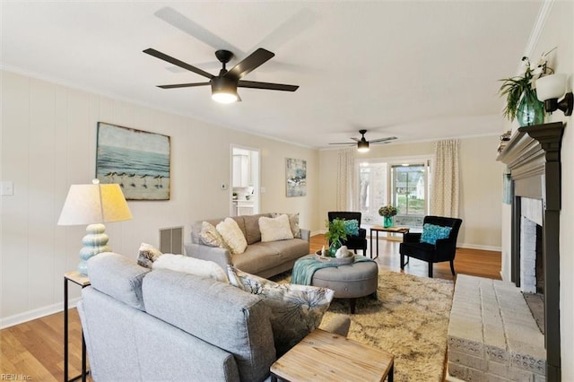 living area with ceiling fan, a brick fireplace, wood finished floors, and ornamental molding