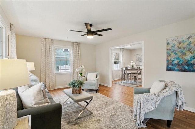 living area featuring wood finished floors, baseboards, and ceiling fan