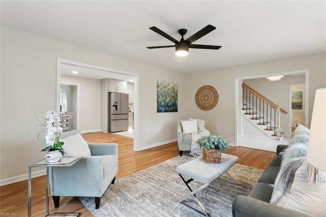 living area featuring ceiling fan, baseboards, light wood-style flooring, and stairs