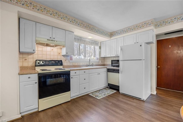 kitchen featuring white appliances, dark wood-style flooring, under cabinet range hood, and a sink