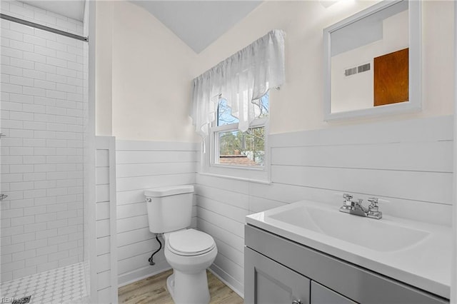 full bath featuring a wainscoted wall, tiled shower, toilet, and visible vents