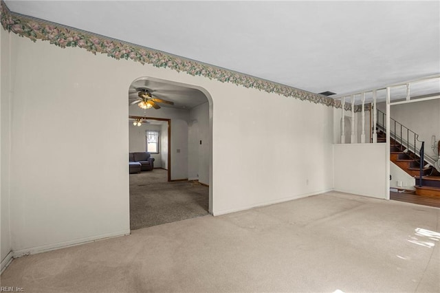 empty room featuring baseboards, carpet, stairway, arched walkways, and a ceiling fan