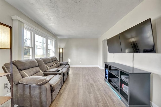 living area featuring baseboards, a textured ceiling, light wood-style flooring, and arched walkways