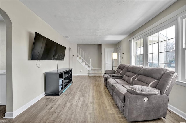 living area with stairway, wood finished floors, arched walkways, and baseboards