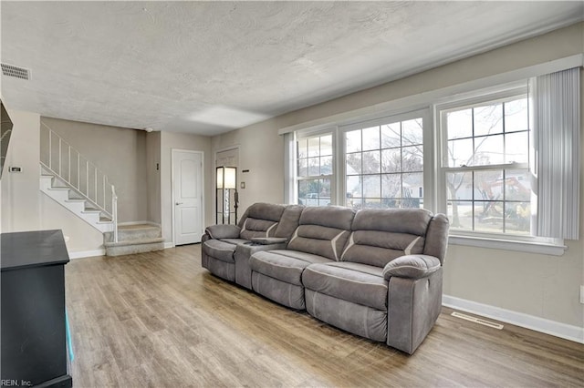 living room featuring plenty of natural light, a textured ceiling, wood finished floors, and stairs