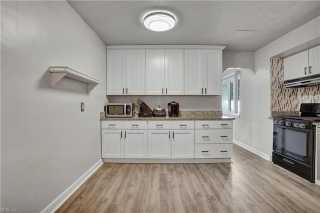 kitchen featuring under cabinet range hood, black gas range, white cabinetry, and stainless steel microwave