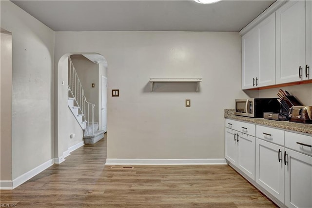 interior space featuring light wood-style flooring, baseboards, and arched walkways