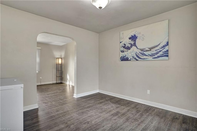 empty room featuring baseboards, arched walkways, and wood finished floors