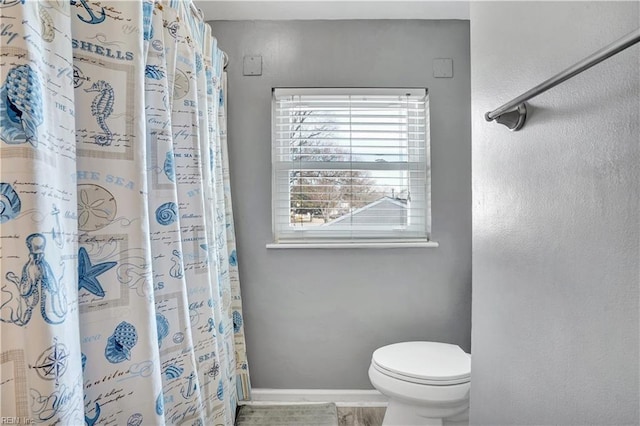 full bath with curtained shower, toilet, and baseboards