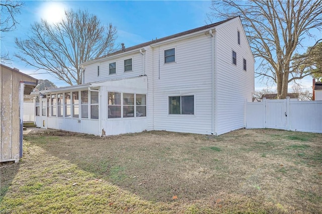 rear view of house featuring a yard, a sunroom, fence, and a gate