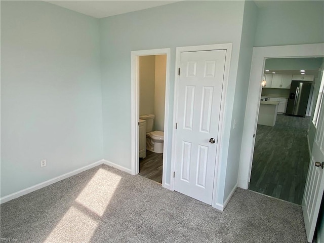 unfurnished bedroom with baseboards, stainless steel refrigerator with ice dispenser, dark carpet, and connected bathroom