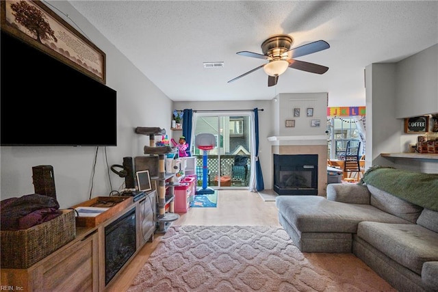 living room featuring a ceiling fan, visible vents, light wood-style floors, a textured ceiling, and a glass covered fireplace