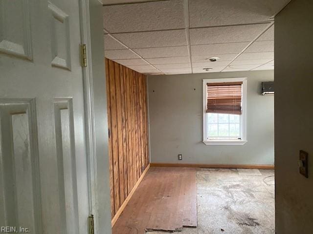 empty room featuring a drop ceiling, wood walls, and baseboards