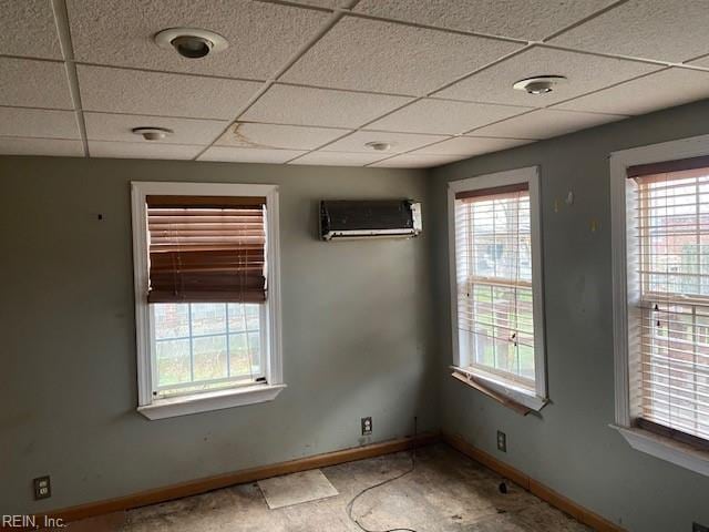 spare room with a drop ceiling, an AC wall unit, and baseboards