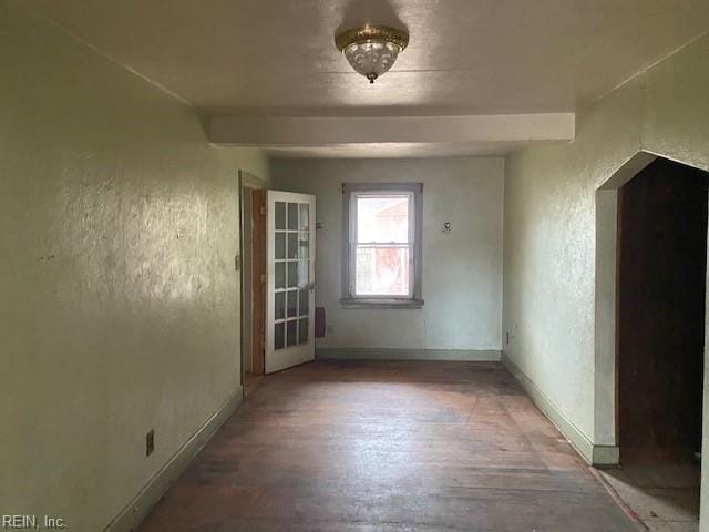 empty room with beamed ceiling, wood finished floors, baseboards, and a textured wall