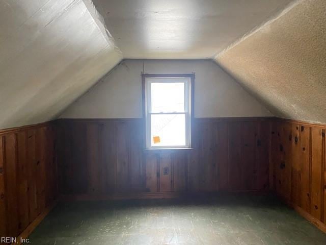 bonus room featuring wooden walls, wainscoting, a textured ceiling, and lofted ceiling