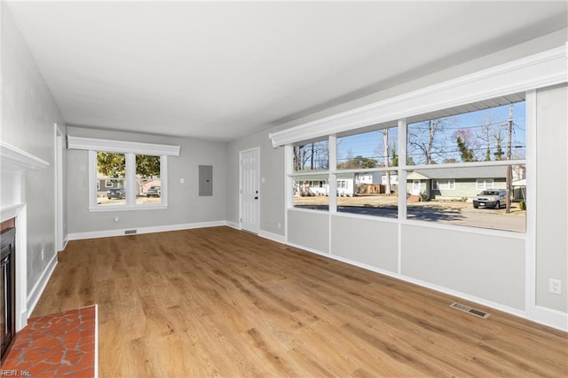 unfurnished living room featuring electric panel, a fireplace with flush hearth, visible vents, and wood finished floors