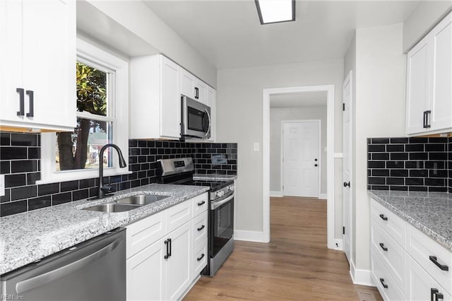 kitchen featuring a sink, white cabinetry, appliances with stainless steel finishes, light wood finished floors, and baseboards