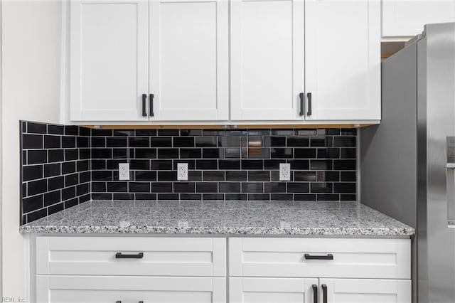 details featuring decorative backsplash, stainless steel fridge, light stone countertops, and white cabinetry