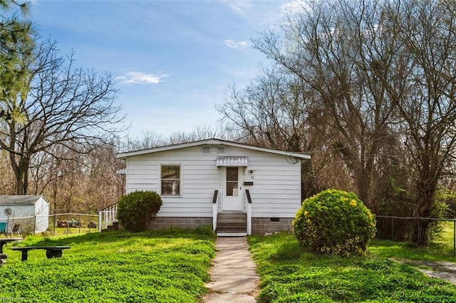 bungalow-style home with entry steps, fence, an outdoor structure, a front yard, and crawl space