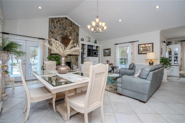 dining space with lofted ceiling, a stone fireplace, french doors, an inviting chandelier, and light tile patterned flooring