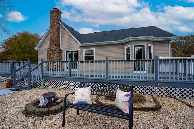 back of property featuring a wooden deck, a fire pit, roof with shingles, and a chimney